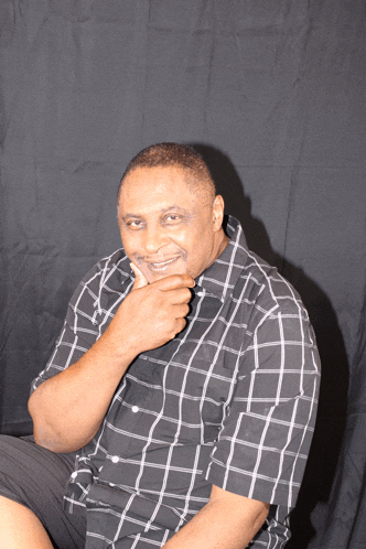 a man wearing a black and white plaid shirt is smiling with his hand on his chin