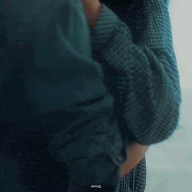 a man and a woman are kissing in front of a window . the woman is wearing a plaid shirt .