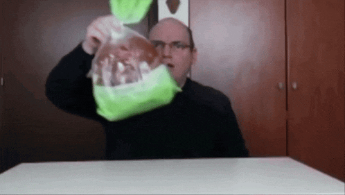 a man with glasses is holding a bag of food over his head