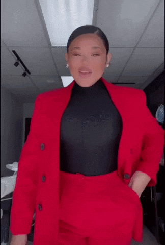 a woman in a red suit and black top is standing in a room with her hands in her pockets .