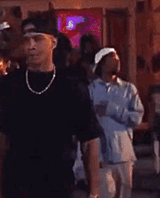 a man wearing a hat and a necklace is standing in a crowd of people