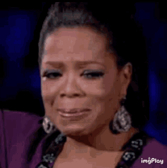 oprah winfrey is crying while wearing a purple dress .