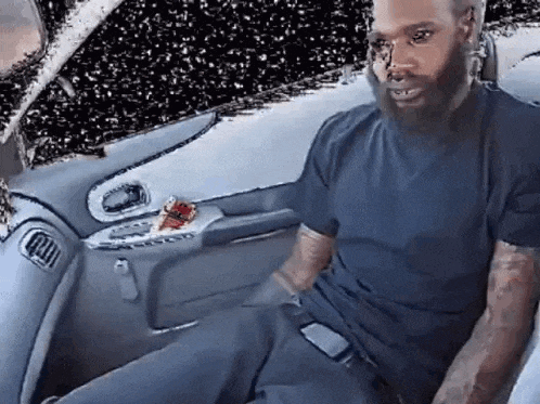a man with a beard is sitting in the back seat of a car talking on a cell phone .