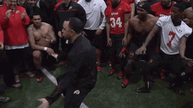 a man is dancing in front of a group of football players one of whom is wearing a utah jersey