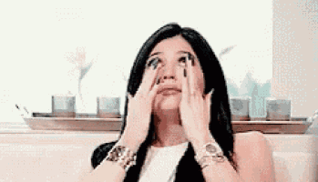 a woman is sitting on a couch and covering her eyes with her hands .