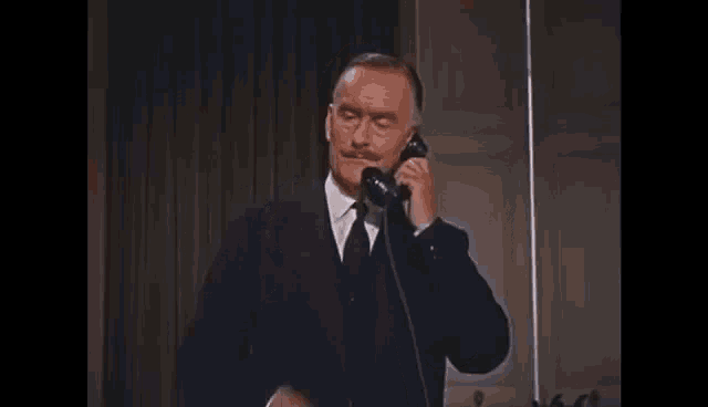 a man in a suit is talking on a telephone .
