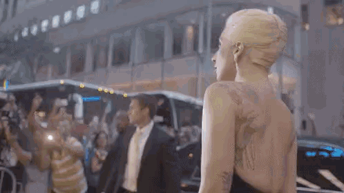a woman with a tattoo on her back is standing in front of a car .