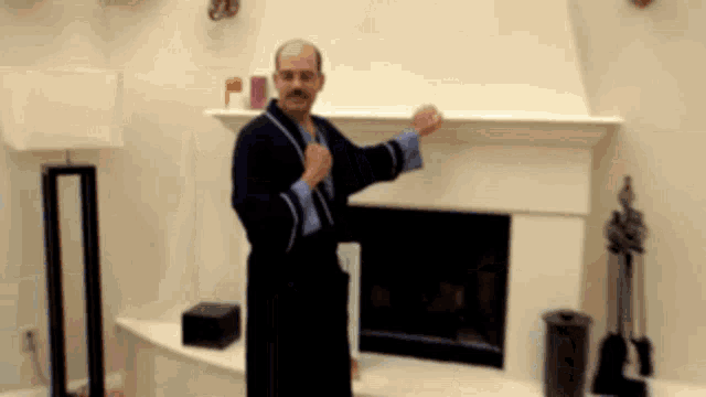 a man in a bathrobe is standing in front of a fireplace