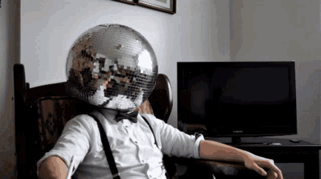 a man with a disco ball on his head is sitting in front of a samsung television