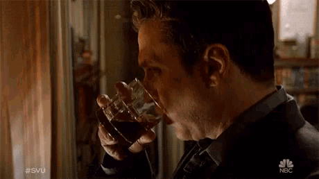 a man drinking a glass of whiskey with the nbc logo in the background