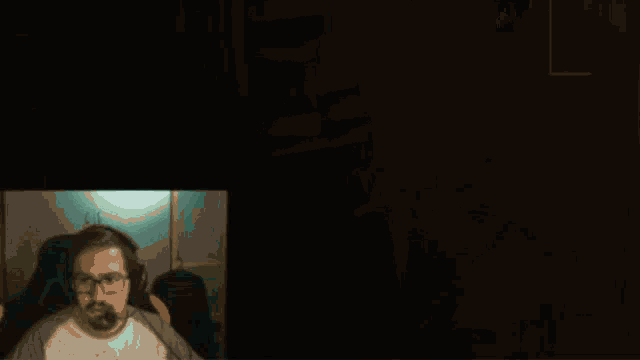 a man wearing glasses and a headset is sitting in front of a bookshelf in a dark room