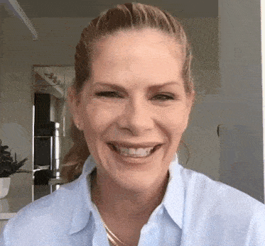 a woman in a blue shirt and gold necklace is smiling