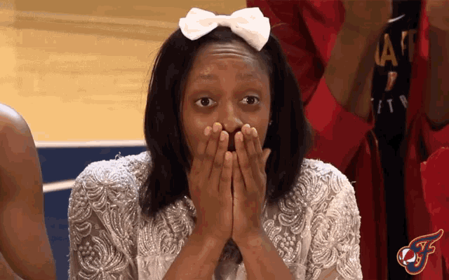 a girl with a bow in her hair is covering her mouth with her hands