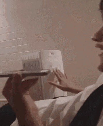 a man in a white shirt and tie is holding a remote control in front of a radiator .