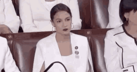 a woman in a white jacket is sitting in a row of chairs in a theatre .