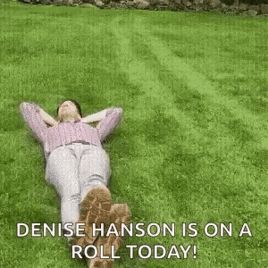 a woman is laying on top of a lush green lawn with the words denise hanson is on a roll today .