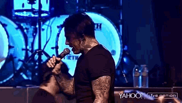 a man is singing into a microphone in front of a drum set with yahoo live nation written on the bottom