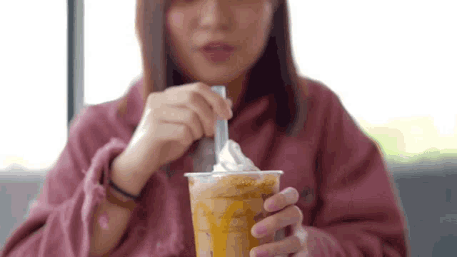 a woman is drinking a milkshake with whipped cream from a plastic cup .