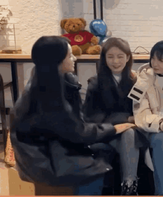 a group of young women are sitting next to each other in a room with a teddy bear in the background .