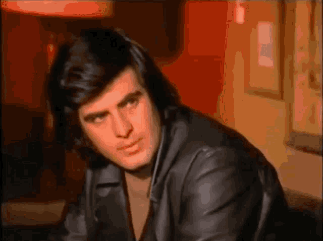 a man in a black leather jacket is sitting in front of a red wall