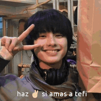 a young man is smiling and making a peace sign with his fingers .