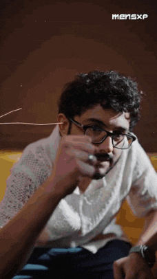 a man wearing glasses is sitting on a couch and holding a string in his ear .