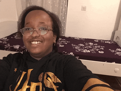 a woman wearing glasses and a black shirt with the letter j on it is smiling