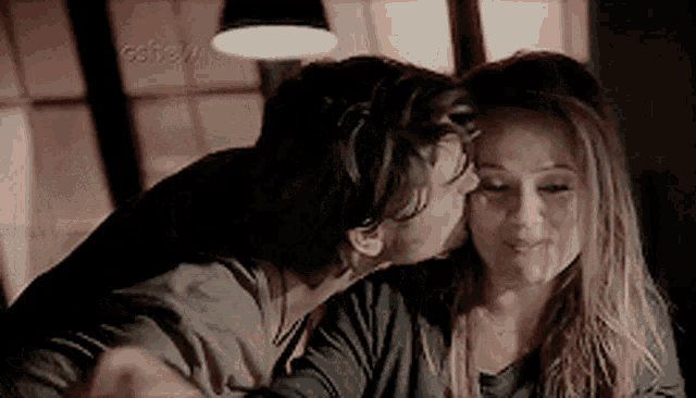 a man kisses a woman on the cheek in front of a sign that says ' cbn ' on it
