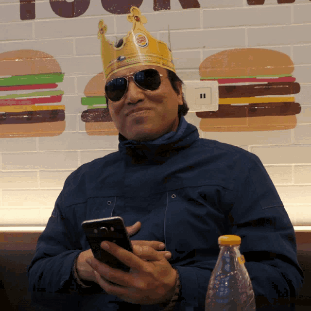a man wearing a burger king crown looks at his cell phone