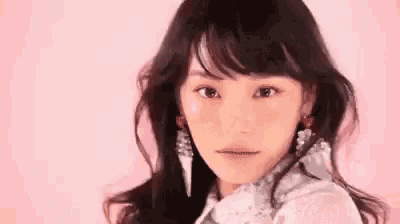 a woman wearing a white lace top and earrings is looking at the camera .