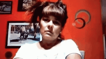 a woman in a white shirt is making a funny face in front of a red wall .