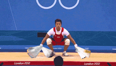a man squatting down with a bag in front of a london 2012 sign