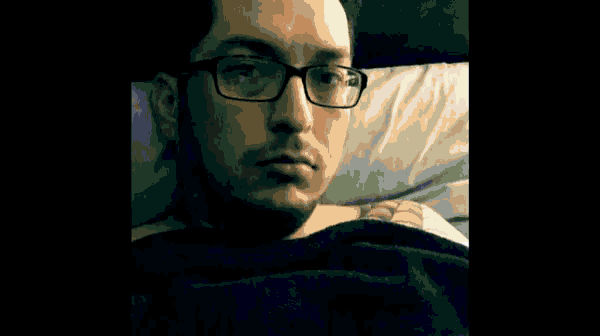 a man with glasses is laying in bed looking at his phone