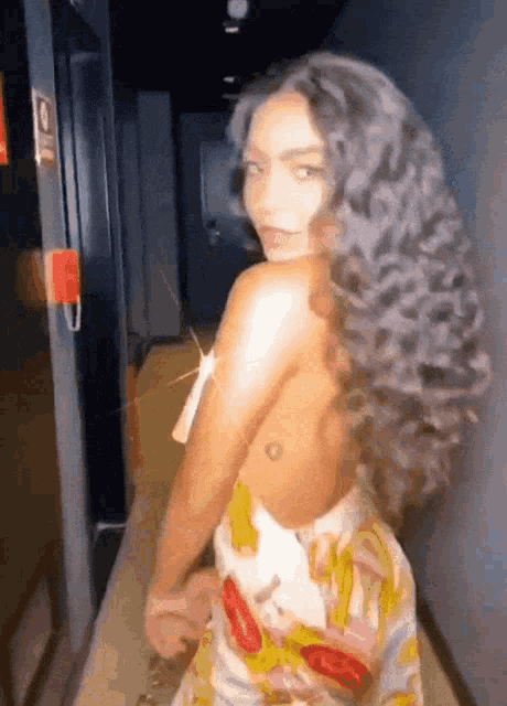 a woman with long curly hair is standing in a hallway .