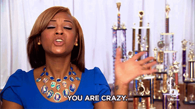 a woman in a blue dress says " you are crazy " in front of trophies