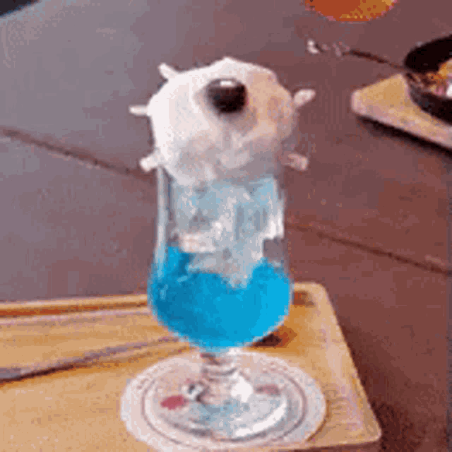 a glass of blue liquid with a white object in it on a wooden table .