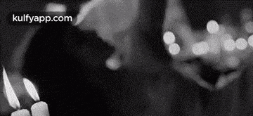 a black and white photo of a person lighting a candle in a dark room .