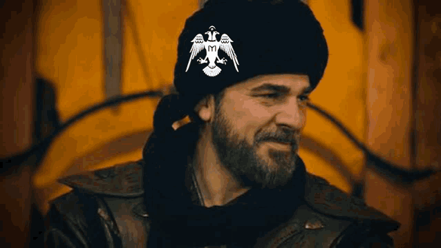 a man with a beard is wearing a black hat with a white eagle on it