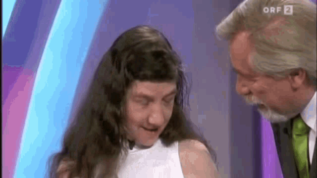 a man in a suit and tie is standing next to a woman with long hair on a television show .