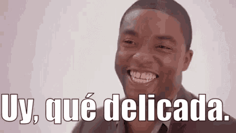 a man in a suit is smiling with the words `` uy , que delicada '' written below him .