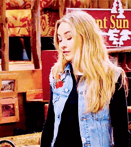 a blonde woman wearing a denim vest stands in front of a sign that says sunset