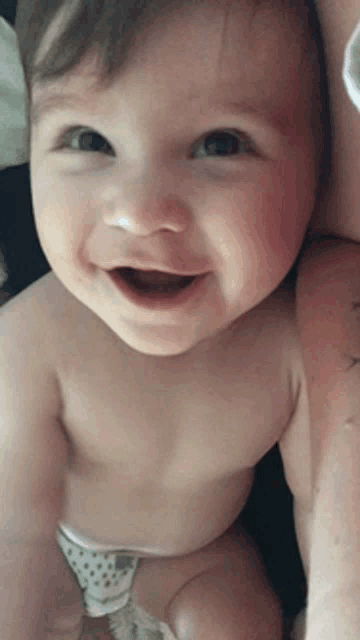 a baby without a shirt is smiling and looking up