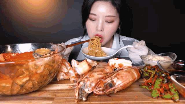 a woman is eating noodles with chopsticks and shrimp on a cutting board