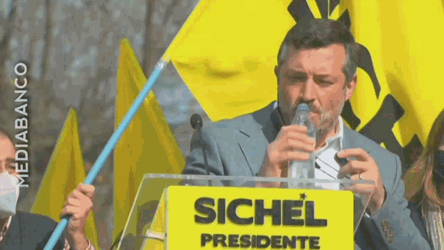 a man stands at a podium with a sign that says sichel presidente