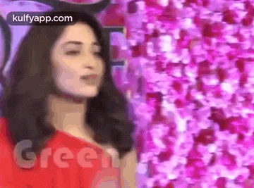 a woman in a red dress is standing in front of a wall of flowers .