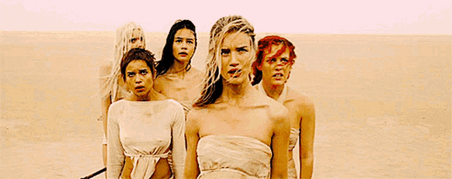 a group of women are standing in the desert and one of them is wearing a white dress
