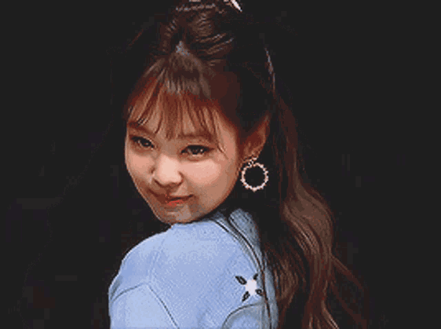 a woman wearing a blue sweater and earrings is smiling for the camera