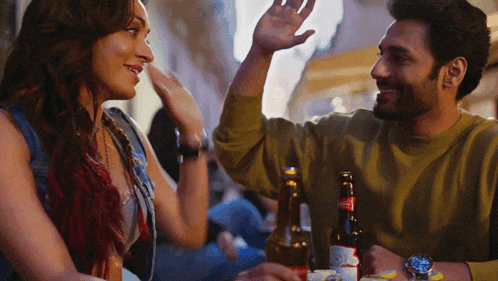 a man and a woman are sitting at a table with a bottle of budweiser in front of them