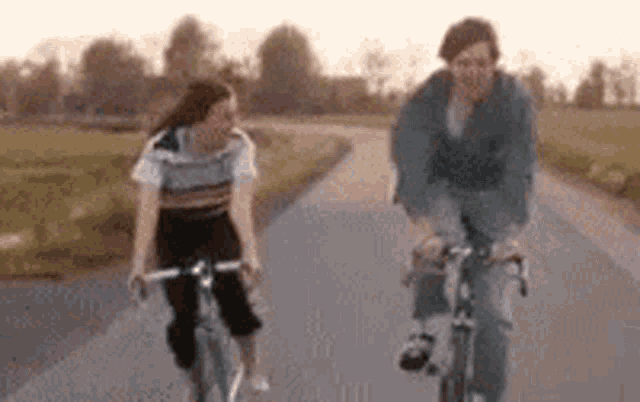two people are riding bicycles down a road .