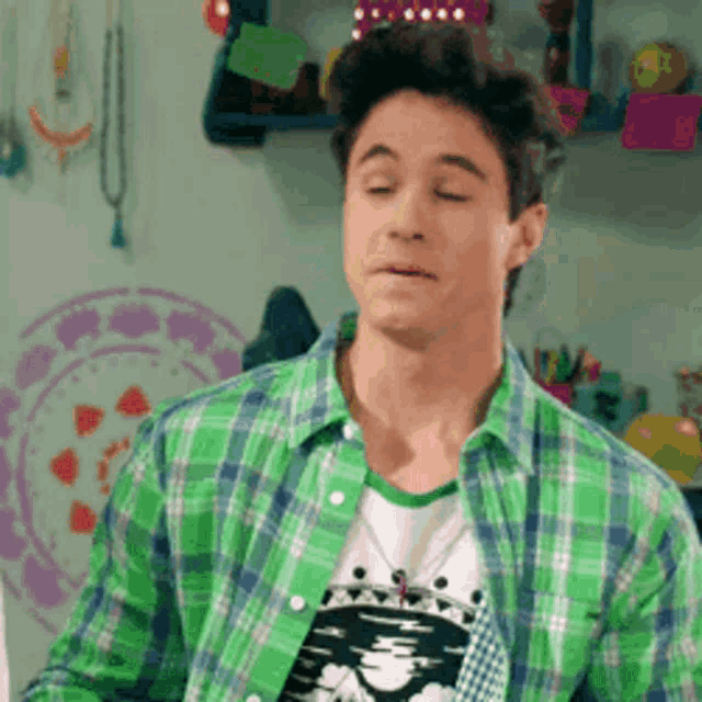 a young man wearing a green plaid shirt and a white t-shirt is making a face .